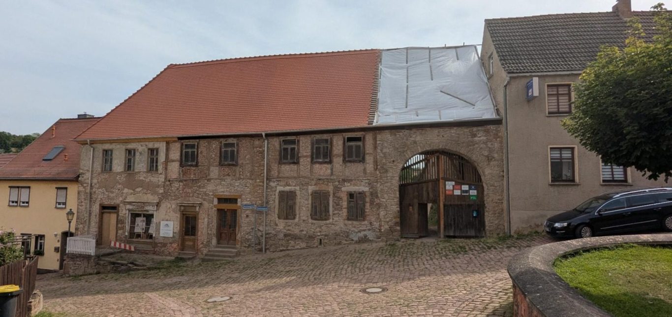 Fassade eines alten, renovierungsbedürftigen Hauses mit Holzfenstern und rotem Dach.